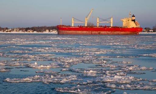 Ice floating on the St. Lawrence near a bulk carrier at anchor in front of a large island with houses on the shore.