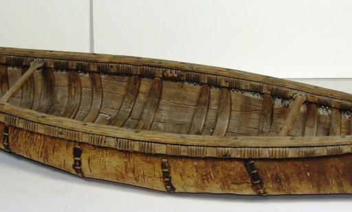 Side view of a canoe showing wooden ribs covered in sheets of birchbark held together by stitching.
