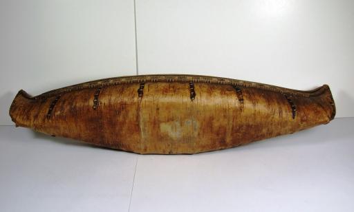 Canoe turned on its side showing smooth bark bottom and stitches sealed with spruce gum on the side. 