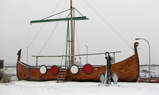 A Viking boat, decorated with red and white circles and bearing a dragon's head on the prow, lies on the snow-covered ground.