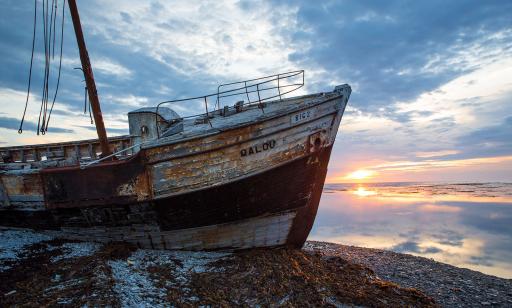 The name Calou can be read on the peeling wooden hull of a wrecked trawler at sunset.