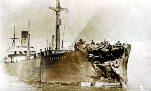 Un navire équipé d’une coque en métal flotte avec des marins à son bord même si sa proue est fortement endommagée.