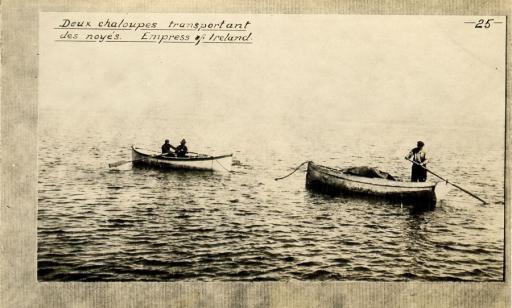 Two men row a boat tied with a cable to another boat, where a man is standing at the stern.