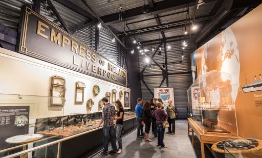 Des visiteurs contemplent des artefacts provenant de l’épave de l’Empress of Ireland ainsi qu’une maquette de ce paquebot.