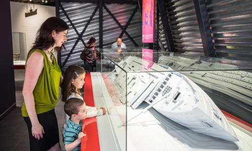 A woman and two children look at a model of the wreck of the ocean liner, lying on its starboard side on the riverbed.