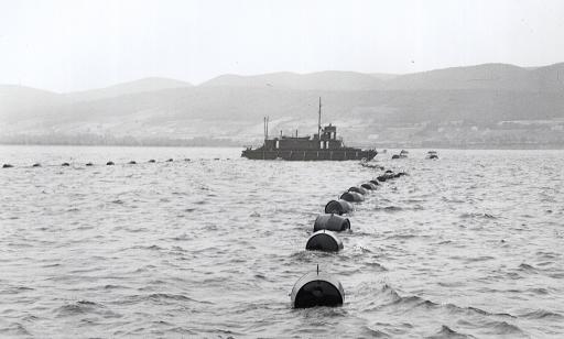 A boat sets up a floating boom used to hold anti-submarine netting in place.