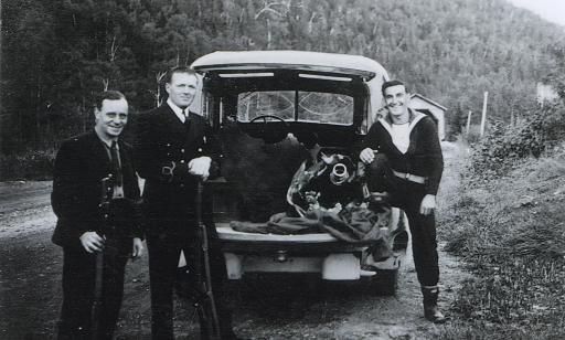 Trois hommes en uniforme, dont deux armés, sont debout près d’un camion dans lequel se trouvent les débris de la torpille.