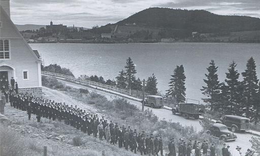 Un grand nombre de civils et de militaires sortent d’une église en faisant une procession derrière le cortège funèbre.