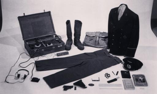 On voit divers objets appartenant à un officier allemand dont un uniforme, un émetteur radio dans une valise et des armes.