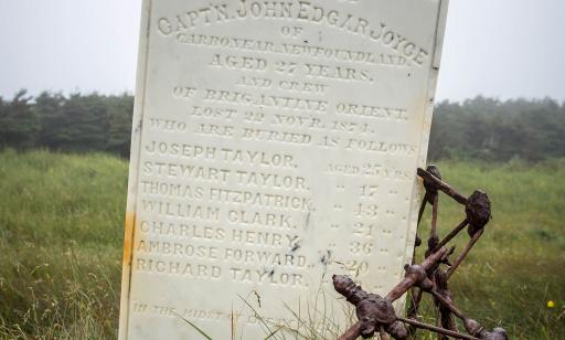 A carved marble tombstone leans against a twisted, rusty iron fence.