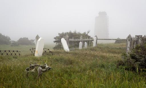 Small cemetery with five crooked tombstones. In the distance, a damaged lighthouse rises through the fog.