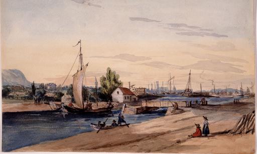 People aboard a small sailboat and a launch on the canal. Many vessels can be seen in the port in the background.