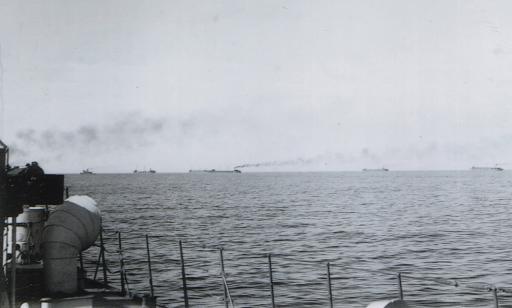Wide view from the deck of a ship showing a line of ships on the horizon, sailing in the same direction.