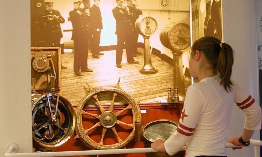 A woman looks at navigational instruments from the wreck, placed in front of a photo of sailors using them.