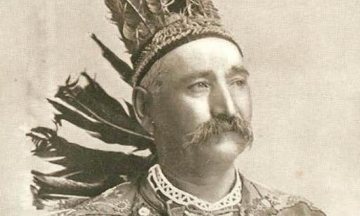 Half length portrait of a Mohawk man wearing a feather headdress and a ceremonial costume embroidered with deer and flowers.
