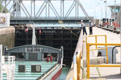 A man throws a cable toward a cargo ship in a lock chamber. The upstream gates of the chamber are shut.