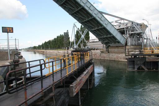 The gates of the lock are halfway open. The bridge is raised at a 45-degree angle and the water level in the chamber and in the canal is the same.