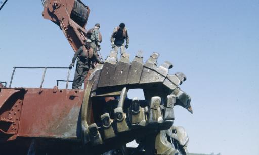 Three men stand on a large cutter suction dredger raised just above the water's surface.