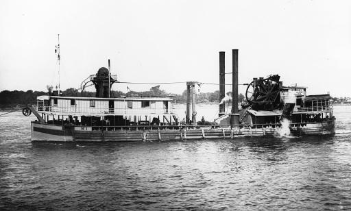 Photo en noir et blanc montrant un navire plat équipé d’instruments pour creuser et extraire les sédiments du fond du fleuve.