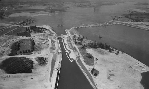 Wide aerial view showing a ship in the canal, another ship in the lock, and the dam.