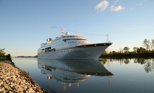 A large white ship with many windows is perfectly reflected in the still water.