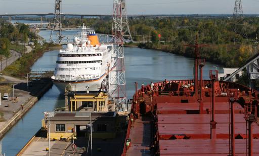 A white ship heads into the open gates of a lock. A red cargo ship sits in the next chamber over.