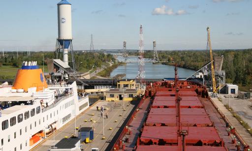 A white ship headed upstream and a red cargo ship headed downstream sit in a lock with two chambers.