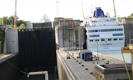 A white ship sailing toward Lake Erie enters the chamber of a lock. The large metal gates are open.