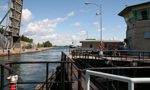 Un navire bleu et blanc se dirige dans un canal vers une écluse dont les portes sont ouvertes et le pont à bascule est levé.