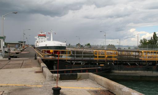 A black, white and red cargo ship sits in the chamber of a lock. The gates are shut. The control building is to the left.