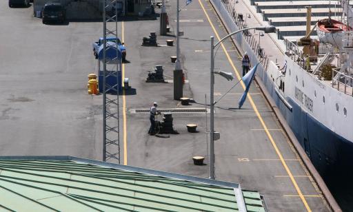 A cargo ship sits in the chamber of a lock, while a man stands near a capstan on the dock, holding a cable.