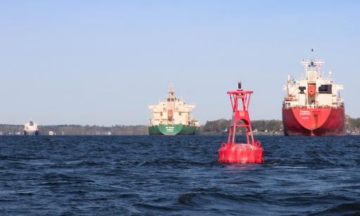 Une photo prise à partir d’un bateau sur le fleuve offre une vue rapprochée d’une bouée rouge et de l’arrière des cargos.