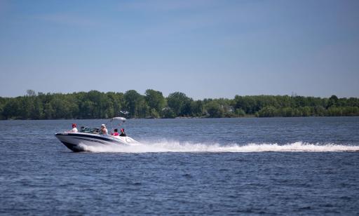 Six people ride in a fast-moving motorboat, leaving a trail of foam in their wake.