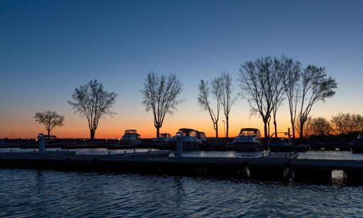 Docks, moored boats and trees can be seen in the dim dawn light against an orange sky.