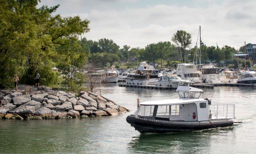 An inflatable excursion boat leaves a marina where many motorboats and a few sailboats are moored.