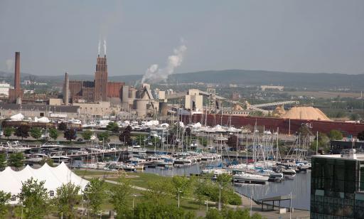 Many sailboats and motorboats are moored at a marina. Port facilities and a train can also be seen.