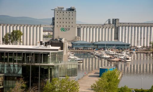 On voit des voiliers et des bateaux à moteur amarrés et, plus loin, des bâtiments du Groupe Océan et d’immenses silos.