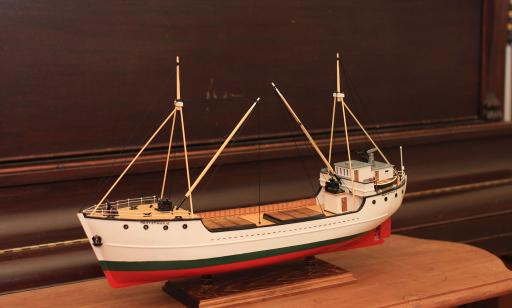 Reproduction miniature d’un bateau en bois, avec des mâts et des hublots, dont la coque est peinte en blanc, vert et rouge.