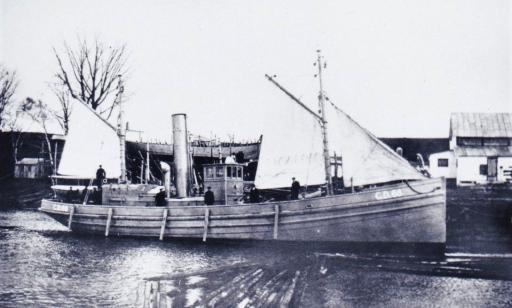 Men aboard a ship bearing two sails in front, another at the back and a smoke stack in the middle.