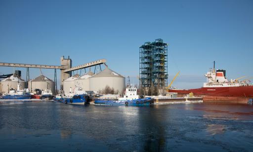 Blue and white boats moored near five steel tanks, two unloading towers and a bulk carrier.