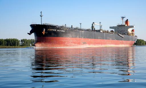 A black and red ship leaves a wake behind it. On the deck, complex cargo pipes can be seen.