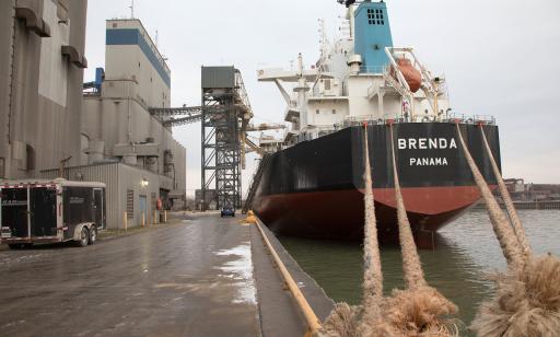 A cargo ship moored at a wharf featuring steel structures, silos and two mobile towers used to unload ships. 