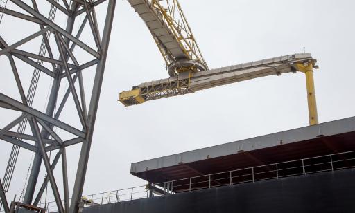 A metal structure on top of a tower is turned toward a cargo ship. A tube descends from it into a hold.