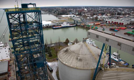 Photo aérienne qui montre une tour en métal près d’un cargo, des réservoirs et au loin un traversier, le port et la ville. 