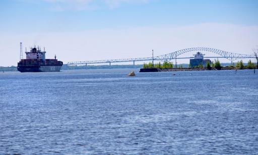 Two large ships heavily loaded with containers sail towards a bridge with a curved centre span.