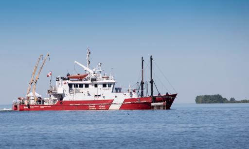 On voit le côté tribord d’un navire rouge et blanc sur le fleuve avec ses appareils de levage et ses instruments de mesure.