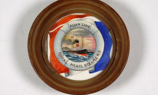 A light brown rim encircles a white, red, blue and black painting of an ocean liner on a decorative plate.