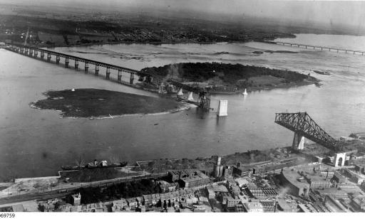 Photo aérienne en noir et blanc qui montre les travaux faits sur le pont et au loin l’île Sainte-Hélène et le pont Victoria.