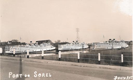 View from the road of three white ships near the shore, in front of several industrial buildings.