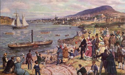 A crowd gathered on the shore watches a small steamboat decked in flags sailing on the river, surrounded by canoes.